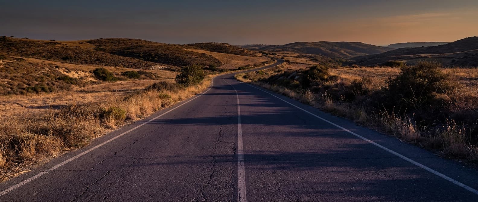 Empty two-lane road crossing dry hills in Cyprus at dusk